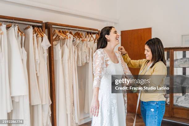 seamstress adjusting the bride's dress in a bridal shop - wedding dress stock pictures, royalty-free photos & images