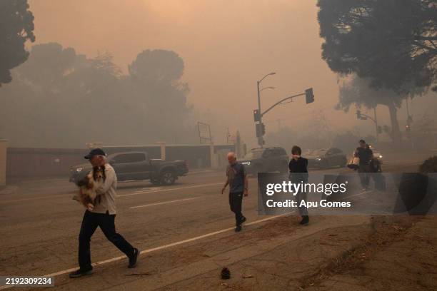 People evacuate along Sunset Boulevard as the Palisades Fire burns amid a powerful windstorm on January 7, 2025 in the Pacific Palisades neighborhood...