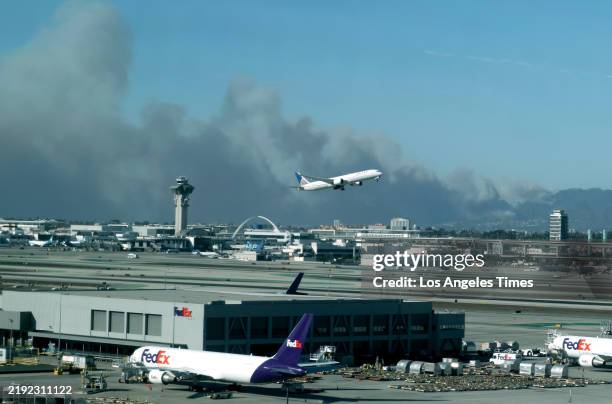 Plane takes off from Los Angeles International Airport in an easterly direction on Tuesday afternoon, January 7 as smoke from a fast-moving brush...