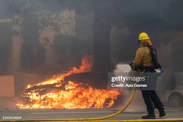 Firefighter sprays water at a burning car on Sunset Boulevard as the Palisades Fire burns amid a powerful windstorm on January 7, 2025 in the Pacific...