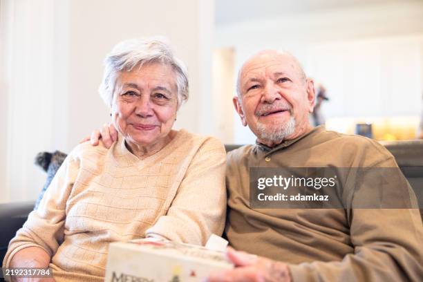 senior couple exchanging gifts on couch - istock photos stock pictures, royalty-free photos & images