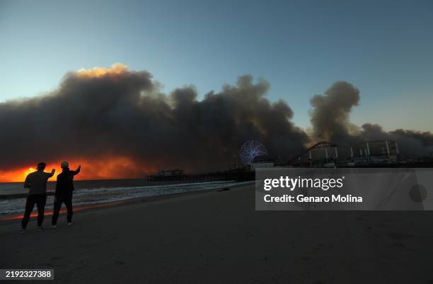 Nick Campbell, left, and friend Joss Glennie-Smith keep a watchful eye on the Pacific Palisades fire that burns several miles behind the Santa Monica...