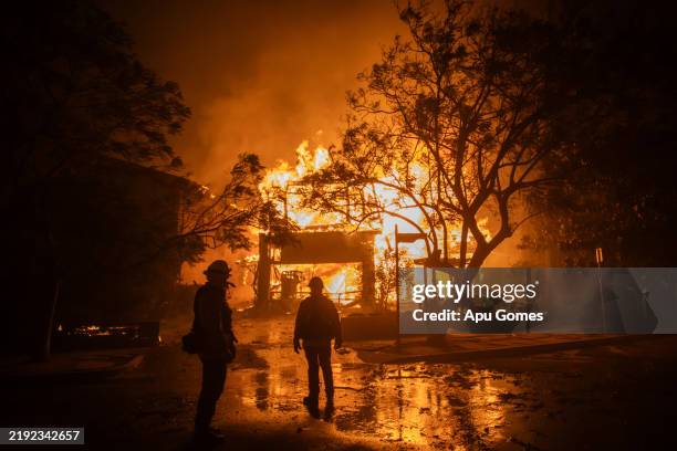 Firefighters watch the flames from the Palisades Fire burning a home during a powerful windstorm on January 8, 2025 in the Pacific Palisades...