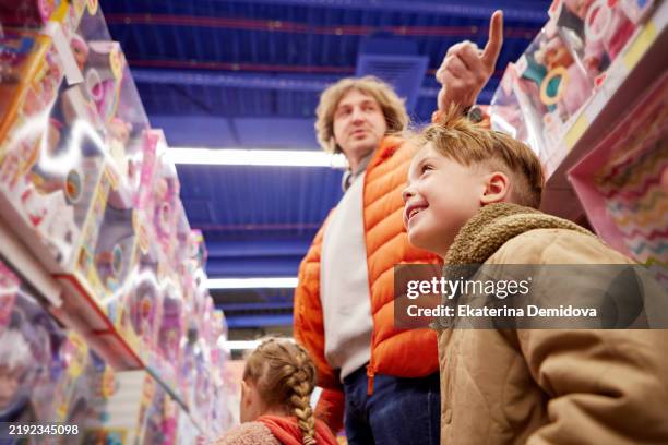 excited children choosing toys with their father in a toy store - loja de brinquedos imagens e fotografias de stock