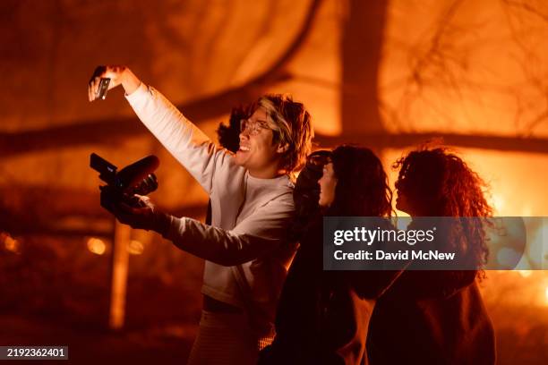 People enter an evacuation zone to take selfie photos and videos near burning homes at the Eaton Fire on January 7, 2025 in Pasadena, California. A...