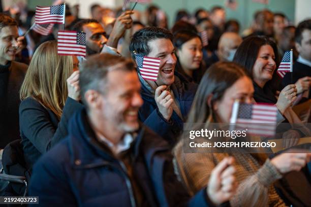 People wave US flags to celebrate becoming US citizens after taking the oath of allegiance during a naturalization ceremony in the jury assembly room...