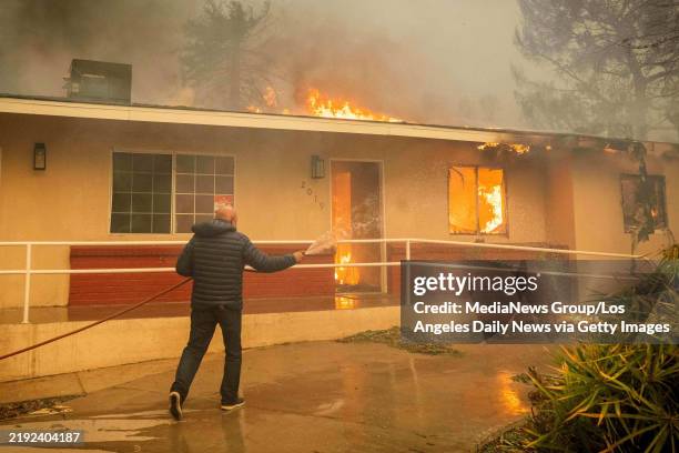 January 08: Csaba Buzy tries to stop a fire at his neighbor's home from spreading to his and other houses on El Molino Avenue in Altadena, CA on...