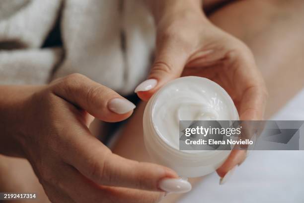 pov women's hands with elegant manicure holding a jar of moisturizing cream , hand and face skin care , anti-aging cream with vitamins and retinol - collagene foto e immagini stock