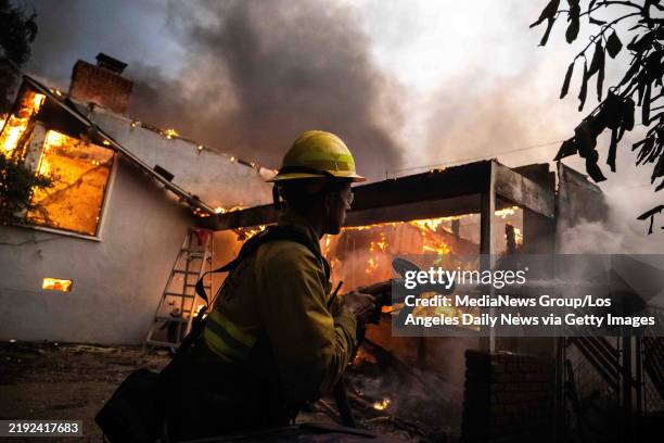 Long Beach firefighter uses water from a pumper truck on Santa Rosa Avenue in Altadena to stop a fire from going to a neighboring house on Wednesday,...