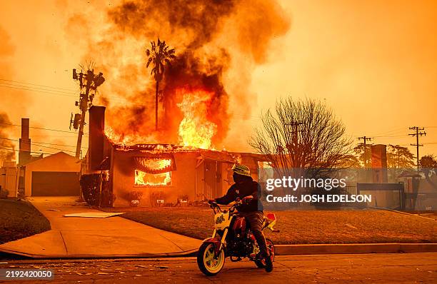 Motorcyclist stops to look at a burning home during the Eaton fire in the Altadena area of Los Angeles county, California on January 8, 2025....