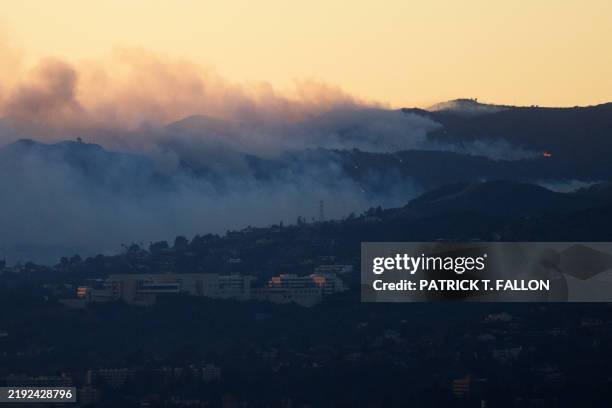 An aerial image shows fire and smoke behind the Getty Center Museum from wildfires, including the Palisades Fire, at sunset over Los Angeles,...
