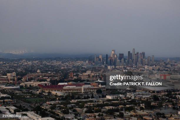 An aerial image shows smoke behind the skyline of downtown Los Angeles, USC campus, and the Los Angeles Memorial Coliseum from wildfires, including...