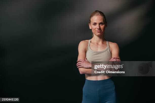 mujer joven segura de sí misma con los brazos cruzados posando sobre fondo oscuro - camiseta de tirantes fotografías e imágenes de stock