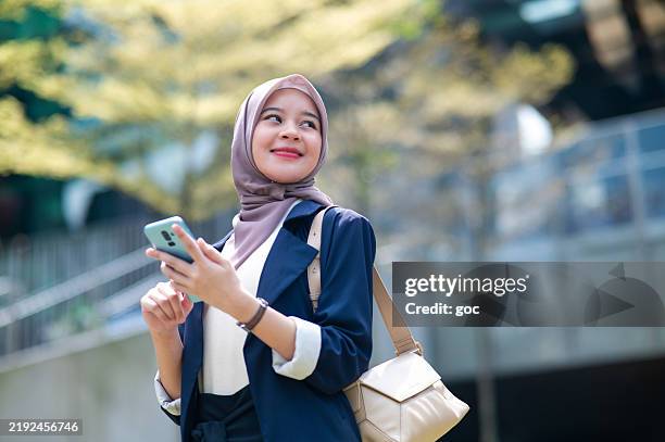 young muslim business woman wearing a hijab and in business casual, using smart phone in the city - asian muslim stock pictures, royalty-free photos & images