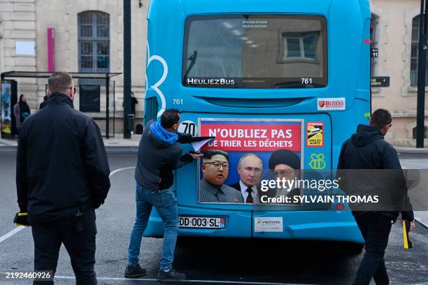 An employee removes a poster from a bus bearing portraits of North Korea's leader Kim Jong Un, Russia's President Vladimir Putin and Iran's Supreme...