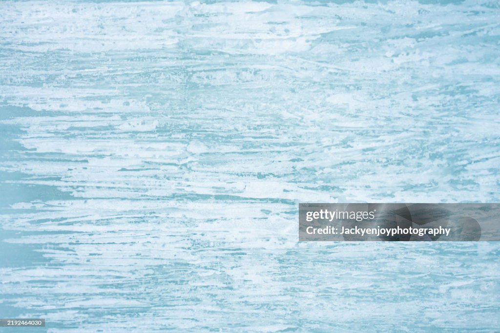 Full-frame image of a river's frozen surface with fractures and shattered turquoise-blue ice crystals.