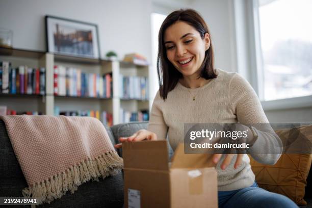 jeune femme excitée déballant sa dernière livraison en ligne à la maison - recevoir photos et images de collection