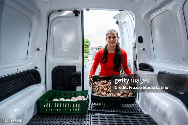 portrait of a young woman putting a box with organic mushrooms into a van - offloading stock pictures, royalty-free photos & images