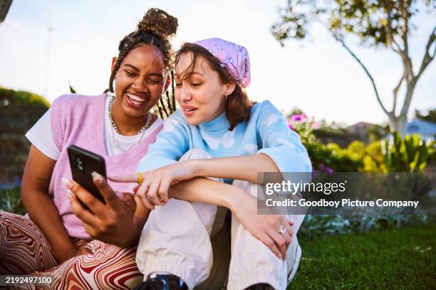 young woman holding smartphone, her friend pointing at screen - een dag uit het leven serie stockfoto's en -beelden