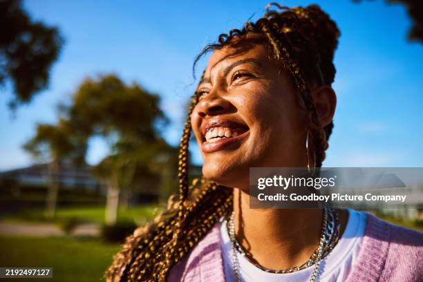 portrait d’une jeune femme aux cheveux tressés regardant ailleurs, sourire à pleines dents - image saisie sur le vif photos et images de collection