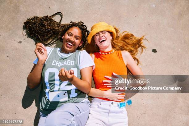 high angle view of two young women lying down on their backs on concrete, laughing - people on their phones stock pictures, royalty-free photos & images