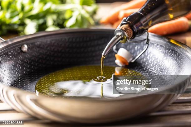 olive oil is poured from a bottle into a modern non-stick frying pan - huile de table photos et images de collection