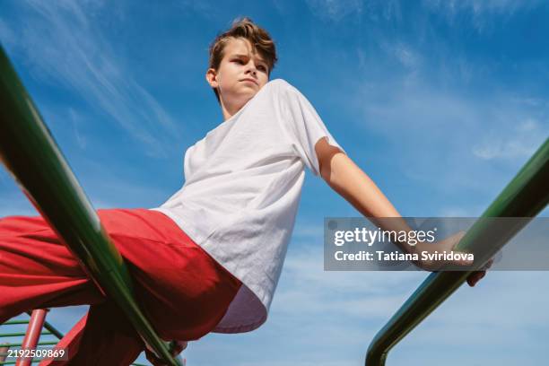 teen boy in sports wear outdoors sits on bars against blue sky - boy blue stock pictures, royalty-free photos & images