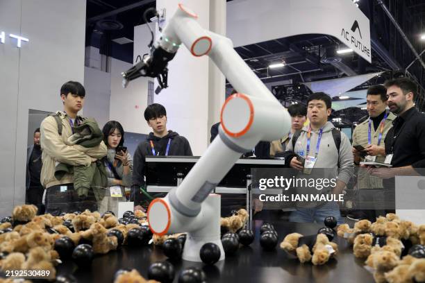 Attendees watch a robotic arm using application development framework to pick up stuffed animals at the Qute booth during the Consumer Electronics...