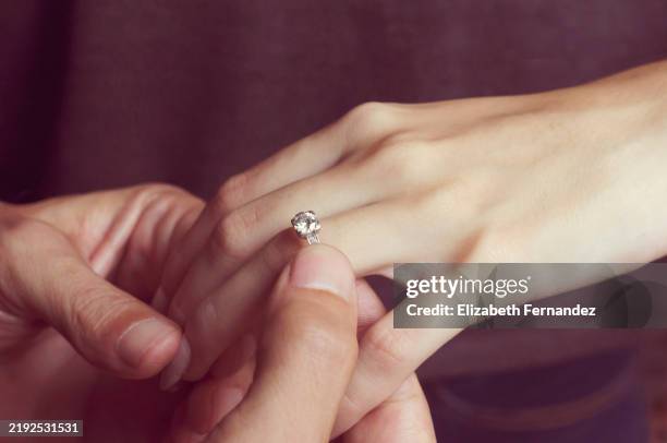 close-up of a man placing a diamond engagement ring on a womans hand, symbolizing love and commitment - bague de fiançailles photos et images de collection