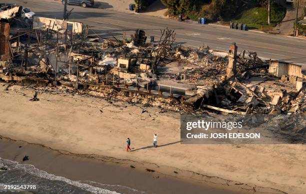 In this aerial view taken from a helicopter, a man waves on the beach in front of burned homes during the Palisades fire in the Malibu, Los Angeles...