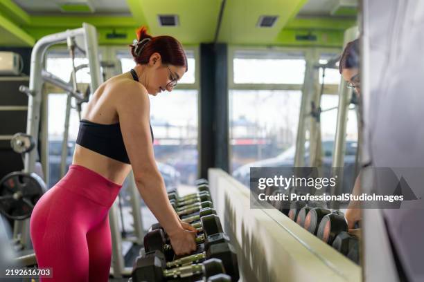 woman preparing for strength training with dumbbells in a modern gym - dumbbell stock pictures, royalty-free photos & images