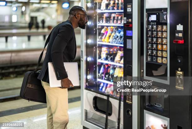 businessman choosing a snack at a vending machine in a train station - verkoopautomaat stockfoto's en -beelden