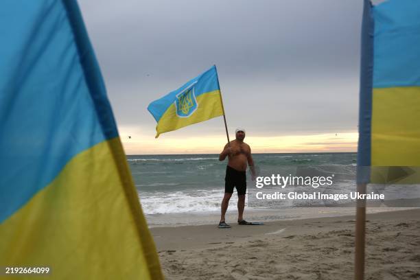 Man poses with flag of Ukraine after plunging freezing water of Black Sea at Lanzheron beach during the Epiphany celebration on January 6, 2025 in...