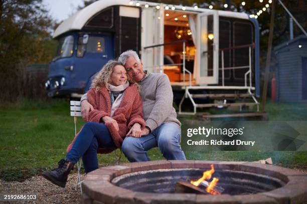 a mature couple sitting together by a campfire - glamping stock-fotos und bilder