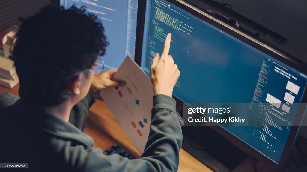 White man programmer or IT specialist software developer working on code examining design based on the visual charts diagrams and design wireframes integrating and development on dual monitors computer