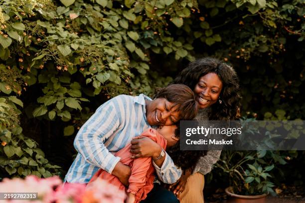 smiling senior woman embracing granddaughter near plants in back yard - familia multigeneracional fotografías e imágenes de stock