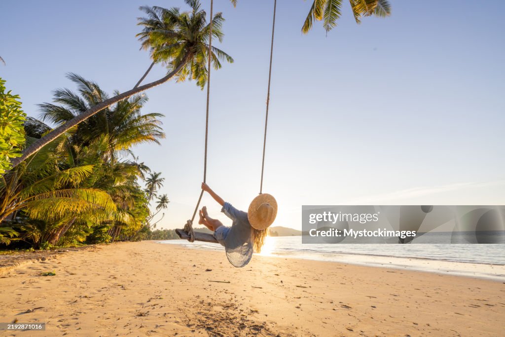 Woman Enjoying a Beach Swing Under Palm Trees