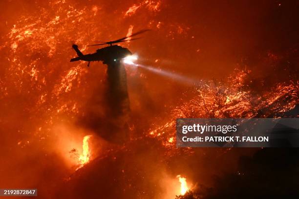 Fire fighting helicopter drops water as the Palisades fire grows near the Mandeville Canyon neighborhood and Encino, California, on January 11, 2025....