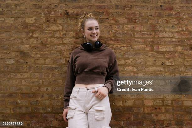 giovane donna sorridente che indossa abbigliamento casual in piedi contro un muro di mattoni all'aperto - pantaloni militari foto e immagini stock
