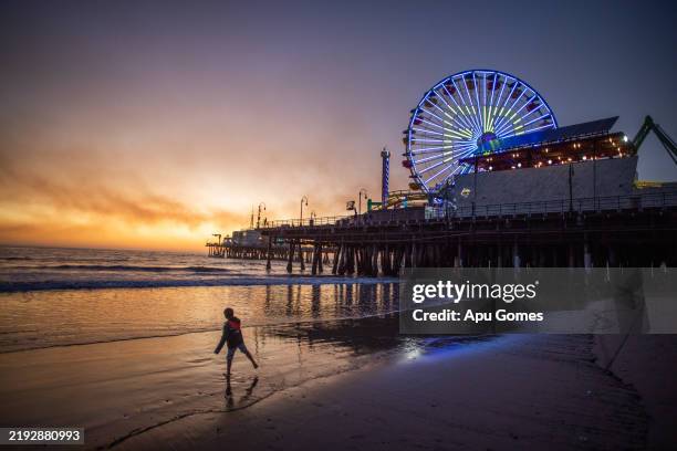 Boy plays on the beach with the Santa Monica pier on the background with smoke from the Palisades Fire seen in the sky on January 11, 2025 in Santa...