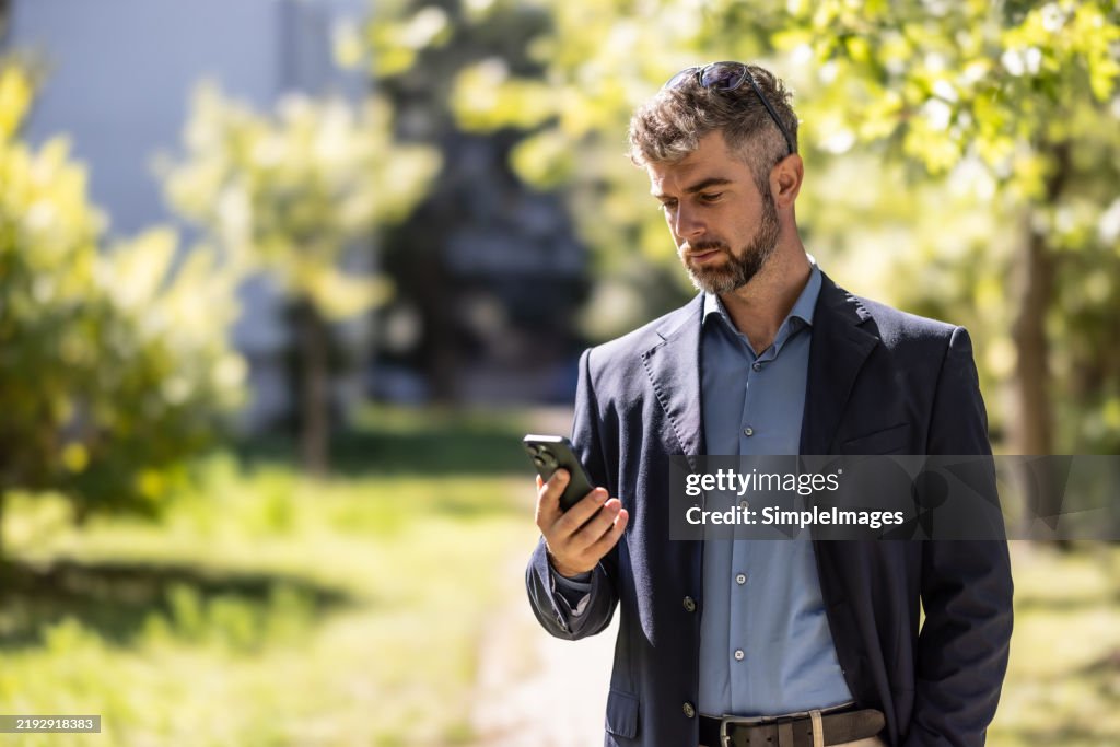 Close up of a smiling businessman, holding smart phone while looking down and reading a message