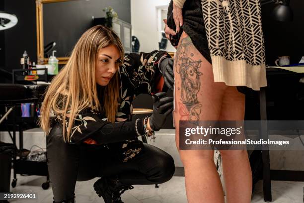 tatoueur créant un motif sur la jambe du client en studio - thigh tattoo photos et images de collection