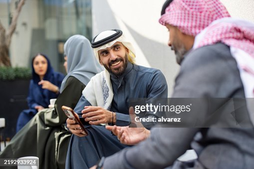 Middle Eastern businessmen in traditional dress discussing over smartphone at coffee break Middle Eastern businessmen in traditional dress discussing over smartphone at coffee break