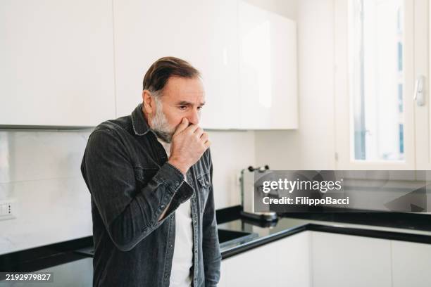 älterer mann hustet in seiner modernen küche - brechreiz stock-fotos und bilder