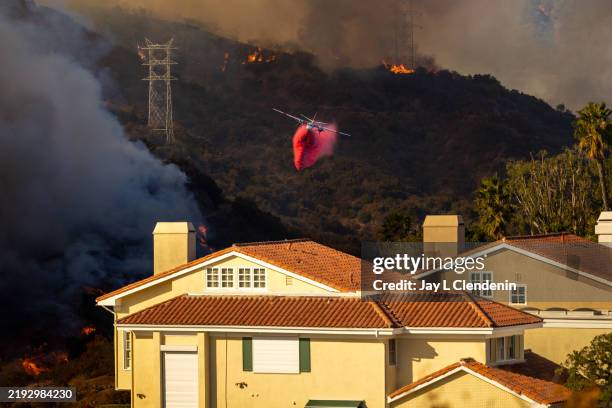 Cal Fire plane drops fire retardant over the Palisades Fire, along Mandeville Canyon, photographed from the Mountaingate development, above...