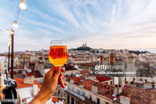 man drinking spritz cocktail at the rooftop bar with the view of marseille old town, french riviera, france - aperol spritz stock pictures, royalty-free photos & images
