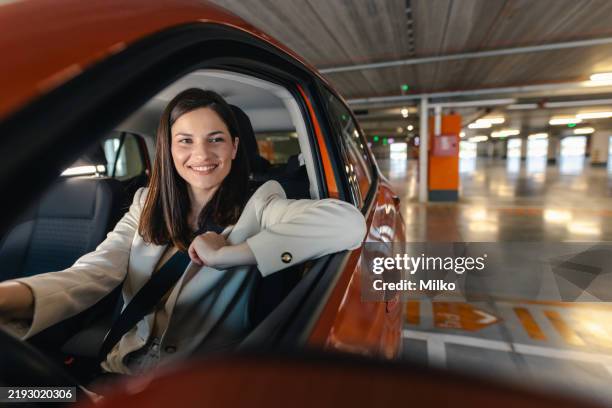 woman driving a car in an indoor parking space confidently and happily - estacionamento de carros imagens e fotografias de stock