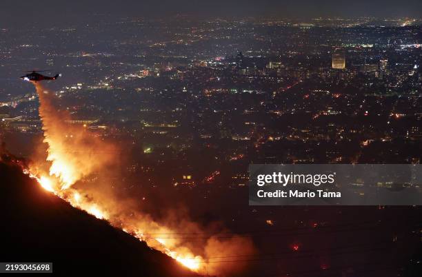 Firefighting helicopter drops water as the Sunset Fire burns in the Hollywood Hills with evacuations ordered on January 8, 2025 in Los Angeles,...