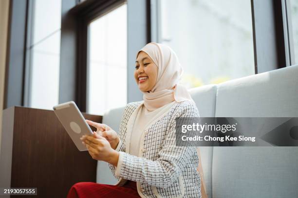 smiling happy asian malay woman working on a tablet in the office. - malay people stock pictures, royalty-free photos & images