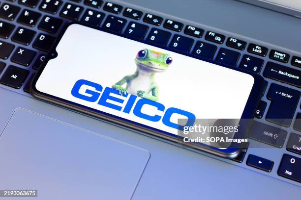 In this photo illustration, the Government Employees Insurance Company logo is seen displayed on a smartphone screen next to a laptop keyboard.